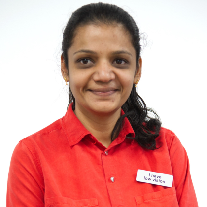 Aarthi is wearing a bright red button up top. She is also wearing a badge that says I am vision impaired.