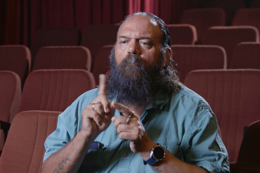 A man sitting in a theatre in the middle of signing a word with his hands.