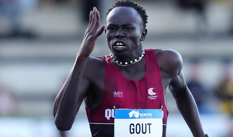 An athlete, in a red shirt, is running a race. The name on his bib says Gout.