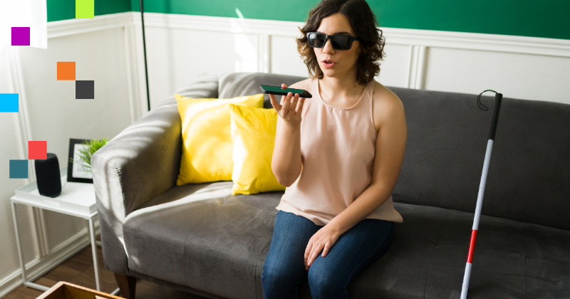 Image of woman wearing shades sitting on a couch. She is holding and speaking into a phone. Beside her, leaning against the couch is a cane.